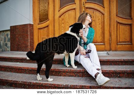 Trendy Girl At Glasses And Ripped Jeans With Russo-european Laika (husky) Dog On A Leash, Against Wo