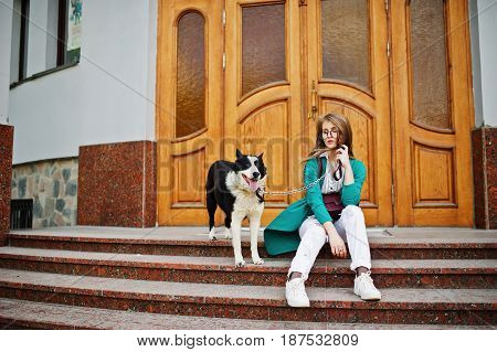 Trendy Girl At Glasses And Ripped Jeans With Russo-european Laika (husky) Dog On A Leash, Against Wo