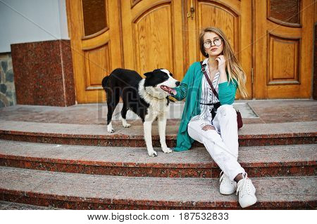 Trendy Girl At Glasses And Ripped Jeans With Russo-european Laika (husky) Dog On A Leash, Against Wo