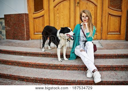 Trendy Girl At Glasses And Ripped Jeans With Russo-european Laika (husky) Dog On A Leash, Against Wo