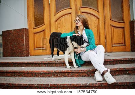 Trendy Girl At Glasses And Ripped Jeans With Russo-european Laika (husky) Dog On A Leash, Against Wo