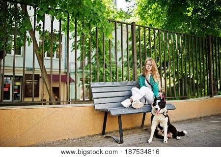 Trendy Girl At Glasses And Ripped Jeans With Russo-european Laika (husky) Dog On A Leash, Against Be