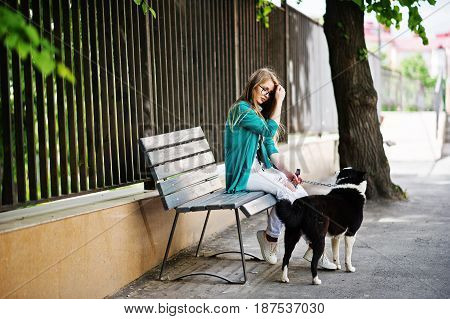 Trendy Girl At Glasses And Ripped Jeans With Russo-european Laika (husky) Dog On A Leash, Against Be