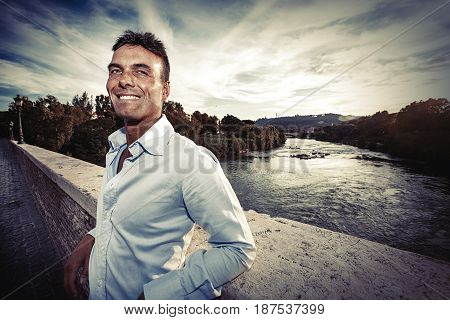 Beautiful smiling man outdoors. Tiber river from the bridge. A beautiful young Italian man posing outdoors on Milvian Bridge in the historic center of Rome, Italy. Blue shirt.