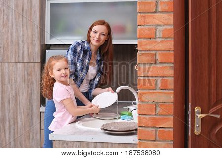 Little girl and her mother doing the washing-up in kitchen at home