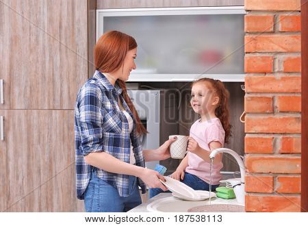 Little girl and her mother doing the washing-up in kitchen at home