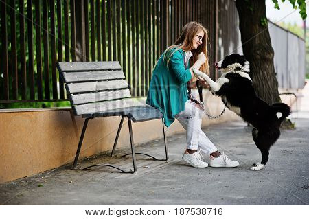 Trendy Girl At Glasses And Ripped Jeans With Russo-european Laika (husky) Dog On A Leash, Against Be