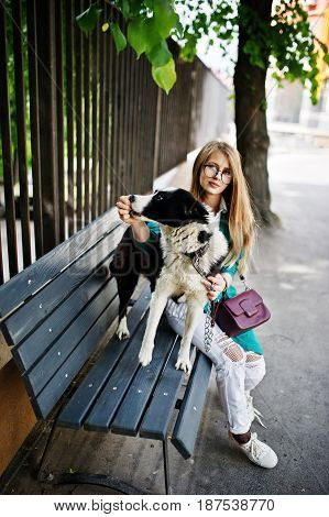 Trendy Girl At Glasses And Ripped Jeans With Russo-european Laika (husky) Dog On A Leash, Against Be