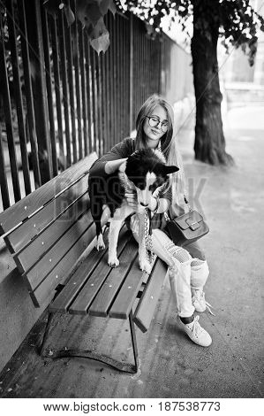 Trendy Girl At Glasses And Ripped Jeans With Russo-european Laika (husky) Dog On A Leash, Against Be