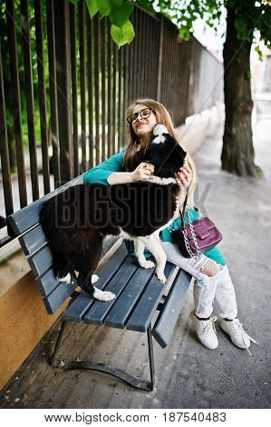 Trendy Girl At Glasses And Ripped Jeans With Russo-european Laika (husky) Dog On A Leash, Against Be