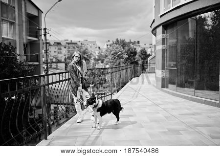 Trendy Girl At Glasses And Ripped Jeans With Russo-european Laika (husky) Dog On A Leash, Against Bu