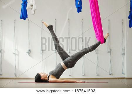 Side view of young woman doing antigravity yoga using hammock in studio. Fitness stretch balance exercise and healthy lifestyle concept. Girl leg supported by material