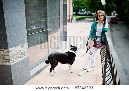 Trendy Girl At Glasses And Ripped Jeans With Russo-european Laika (husky) Dog On A Leash, Against Bu