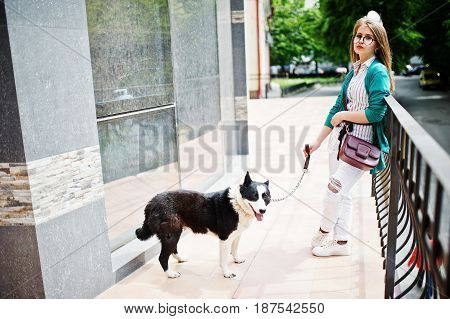 Trendy Girl At Glasses And Ripped Jeans With Russo-european Laika (husky) Dog On A Leash, Against Bu