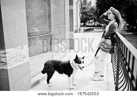 Trendy Girl At Glasses And Ripped Jeans With Russo-european Laika (husky) Dog On A Leash, Against Bu