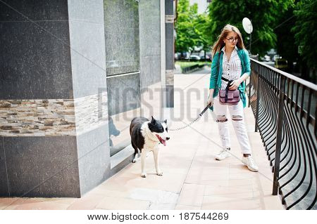 Trendy Girl At Glasses And Ripped Jeans With Russo-european Laika (husky) Dog On A Leash, Against Bu