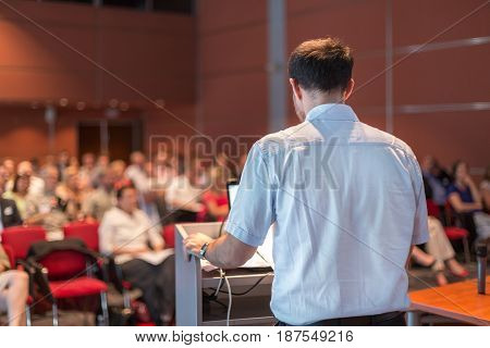 Casualy dressed professor giving talk at scientific conference. Audience at the conference hall. Research experts and entrepreneurship event.