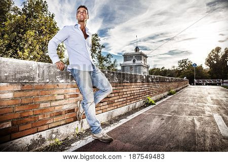Handsome smiling man outdoors. Tiber river from the bridge. A beautiful young Italian man posing outdoors on Milvian Bridge in the historic center of Rome, Italy. Blue shirt and jeans.
