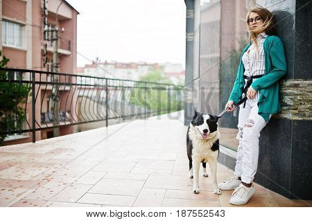 Trendy Girl At Glasses And Ripped Jeans With Russo-european Laika (husky) Dog On A Leash, Against St