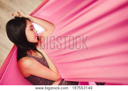 Girl dreaming and meditation in pink silk lighted hammock hanging in relaxed position. Antigravity yoga training in bright gym studio. Aero yoga trainer does exercises