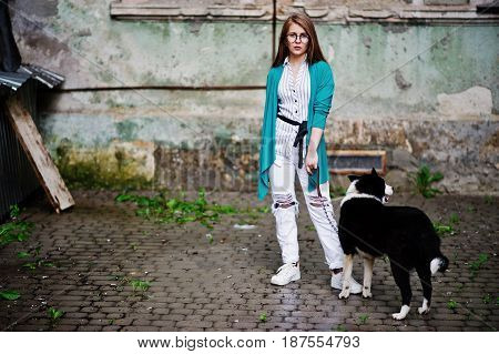 Trendy Girl At Glasses And Ripped Jeans With Russo-european Laika (husky) Dog On A Leash, Against St