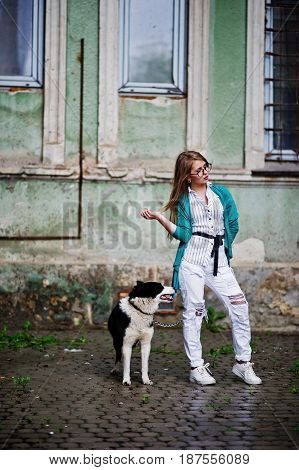 Trendy Girl At Glasses And Ripped Jeans With Russo-european Laika (husky) Dog On A Leash, Against St