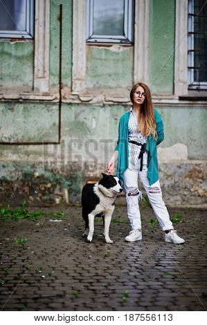 Trendy Girl At Glasses And Ripped Jeans With Russo-european Laika (husky) Dog On A Leash, Against St