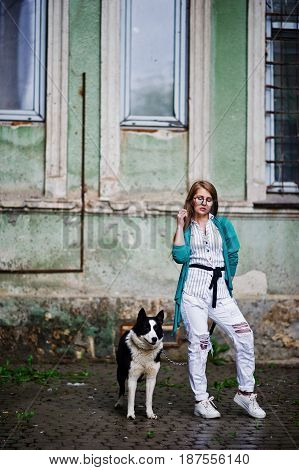 Trendy Girl At Glasses And Ripped Jeans With Russo-european Laika (husky) Dog On A Leash, Against St