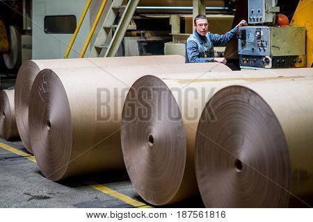Paper mill factory worker operating equipment near paper rolls