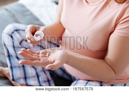 Healthy pregnancy. Expectant mom sitting on a bed with her legs crossed and taking some vitamins.