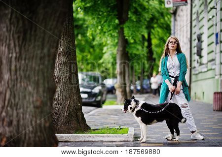 Trendy Girl At Glasses And Ripped Jeans With Russo-european Laika (husky) Dog On A Leash, Against St