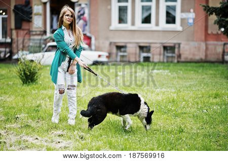 Trendy Girl At Glasses And Ripped Jeans With Russo-european Laika (husky) Dog On A Leash, Against St