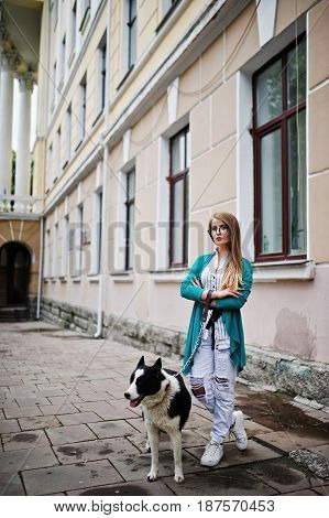 Trendy Girl At Glasses And Ripped Jeans With Russo-european Laika (husky) Dog On A Leash, Against St