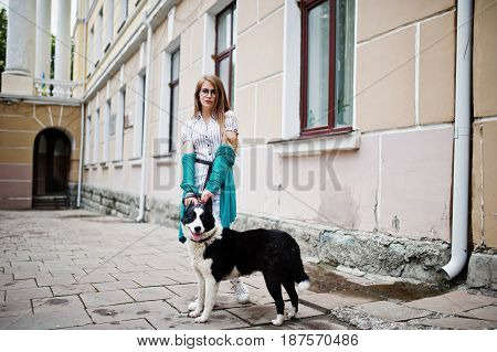 Trendy Girl At Glasses And Ripped Jeans With Russo-european Laika (husky) Dog On A Leash, Against St