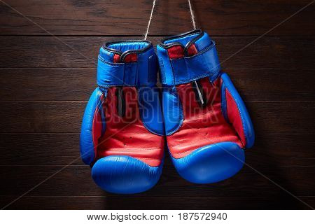 Boxing blue and red gloves hanging from ropes on a wooden background. Horizontal photo of the bright sportwear against brown wall. Boxing backgrounds and still-life. Concept of the active lifestyle.