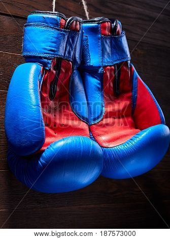 A pair of red and blue boxing gloves hang against wooden wall. Vertical photo of the bright colorful sportwear against brown background. Boxing backgrounds and still-life. Sportive exercise and training. Concept of the active lifestyle.