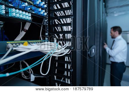 Information center. Selective focus of internet wires being connected to the patch panel with a handsome male technician working in the background