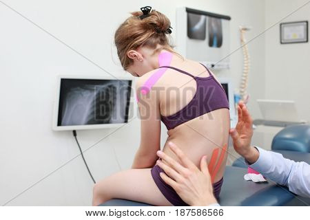 specialist performing  kinesio taping application m girl's shoulder and back in office