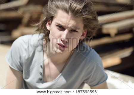Portrait of young handsome man over wood boards, outdoor. Attractive trendy fashion 18 years old teen boy posing outside over construction waste, image toned.