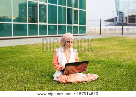 A young muslim woman using laptop outdoors.