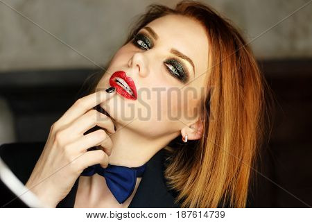 Young attractive girl in a jacket and bow tie looks languidly. Femme fatale. Evening makeup smokey eye. Lust.