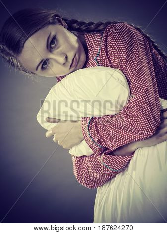 Mental health depression insomia concept. Sad depressive young woman teen blonde girl wearing red pajamas sitting on bed embracing pillow on grey wall background