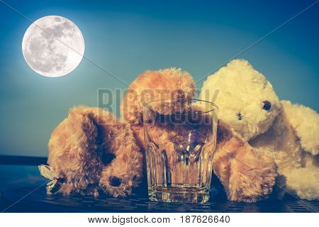 Teddy bears couple very drunk alcoholic and sleeping with empty glass on table blue sky and full moon background. Alcohol is not good for health and don't drink concept. Vintage effect tone.