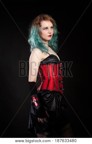 Slim woman in fetish red leather corset on black background in studio photo. BDSM and dominatrix