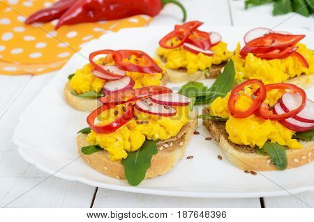 Sandwich with scrambled eggs rucola radish paprika kapi and flax seeds on a plate on a white wooden background. Fast and tasty breakfast. Close up