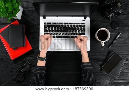 Business and technology topic: the hand of woman in a black shirt showing gesture against a black and white background laptop at the desk. Top view