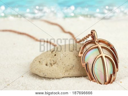 Golden jewellery pendant on summer sand beach with sea background soft focus