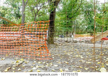 Confined space with orange plastic safety net is placed around the building site in deciduous park.