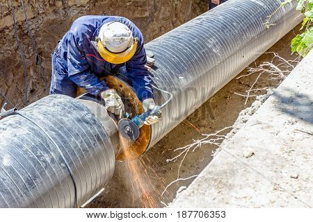 Worker is cleaning welding seam on pipeline with a grinding machine. Preparation for welding
