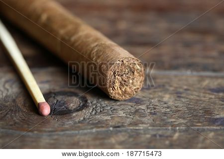 One Cuban cigar near matchstick on old wooden board